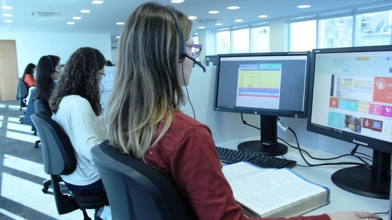 Quatro consultoras em uma sala usanso fones de ouvido, sentadas em frente aos computadores para realizar o atendimento em telessaude